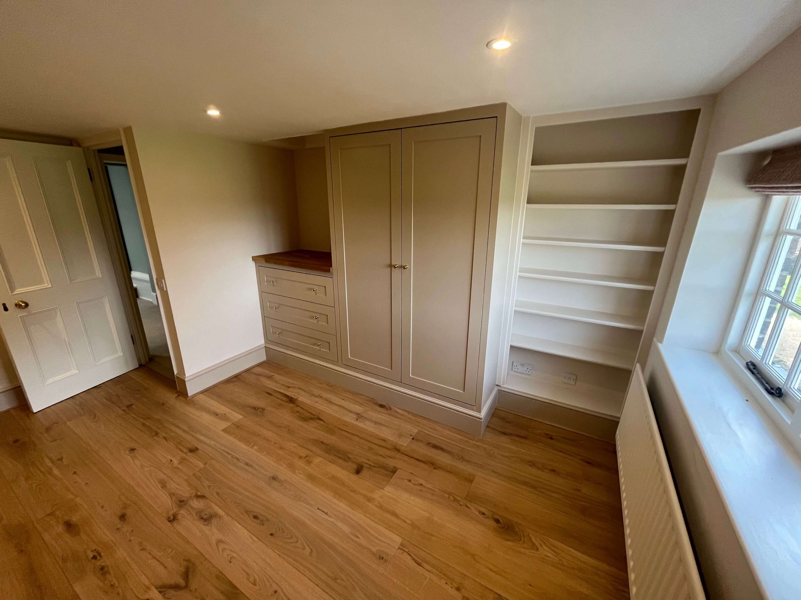 Services Fitted bedroom wardrobe in painted greige with oak-topped drawer unit and alcove shelving, on an oak floor