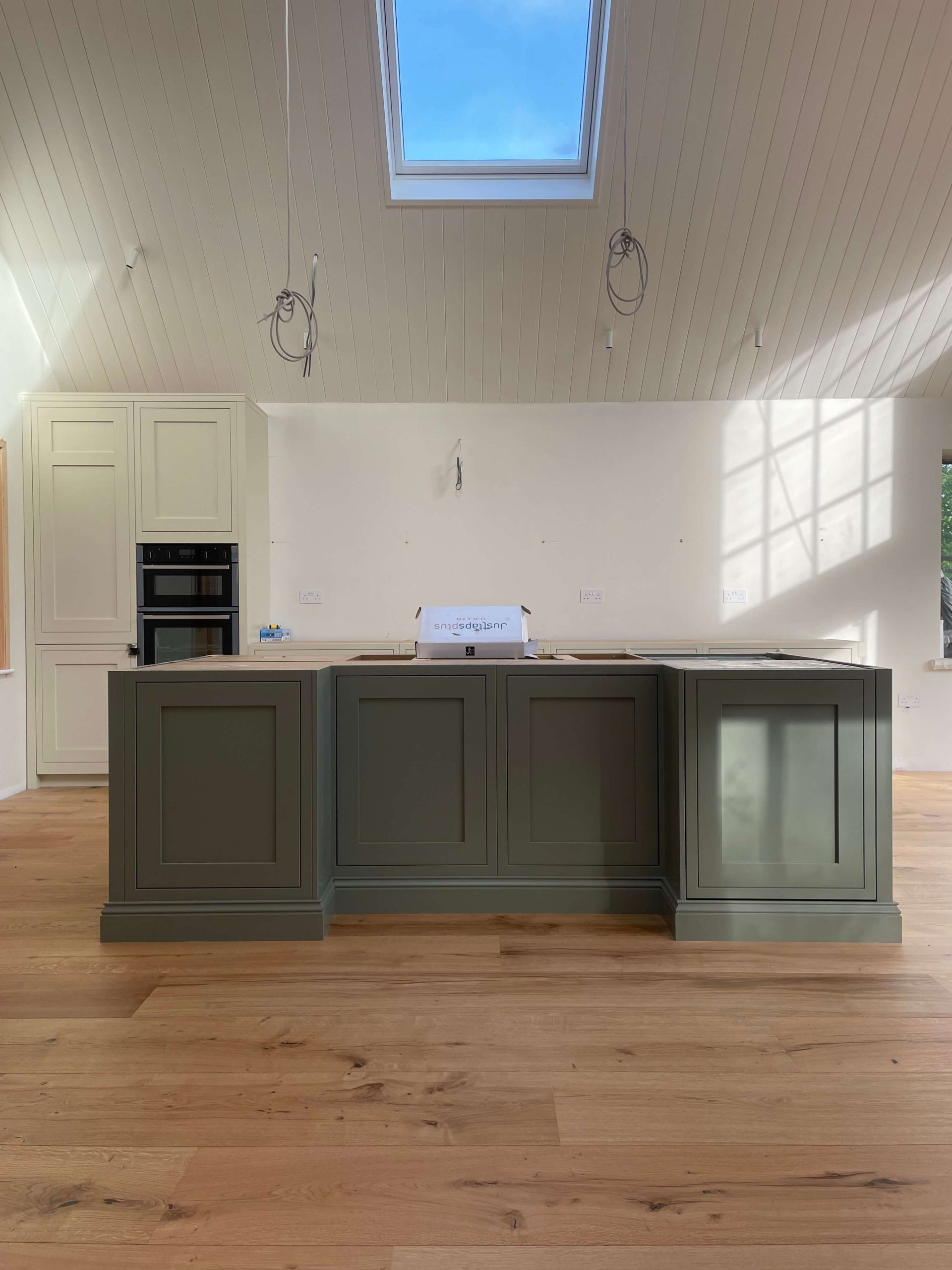 Home Kitchen island in deep green with shaker panelling, under a vaulted timber-lined ceiling